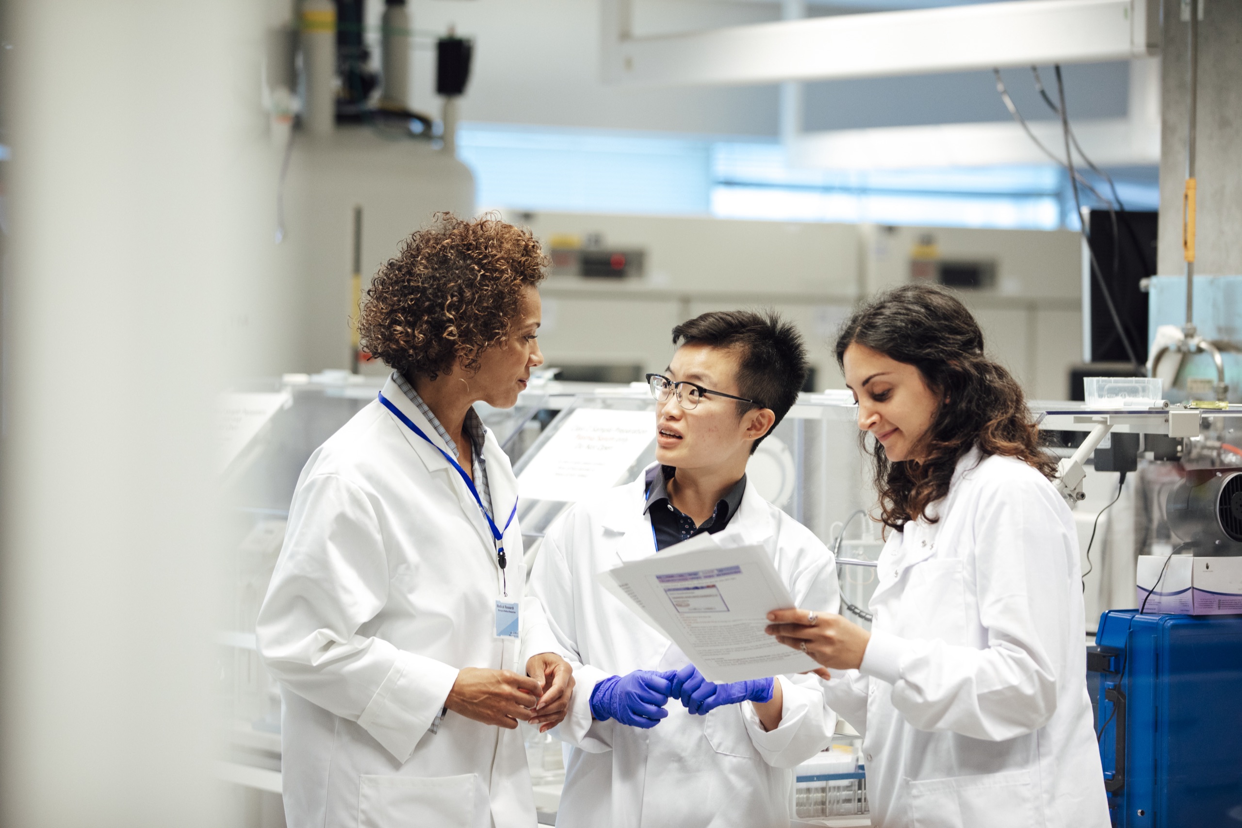 Three researchers in lab coats reviewing a document together